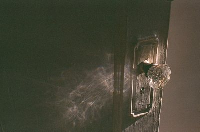 Dark photograph of an old doorknob and lock on a green painted door.