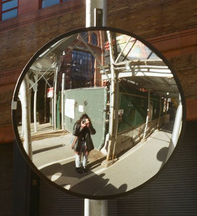 Self-portrait reflected in a convex traffic mirror on a city street.