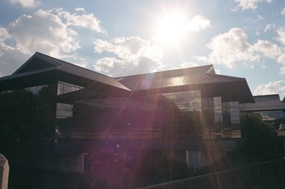 Photograph of the sun flaring over the roofline of a low building.